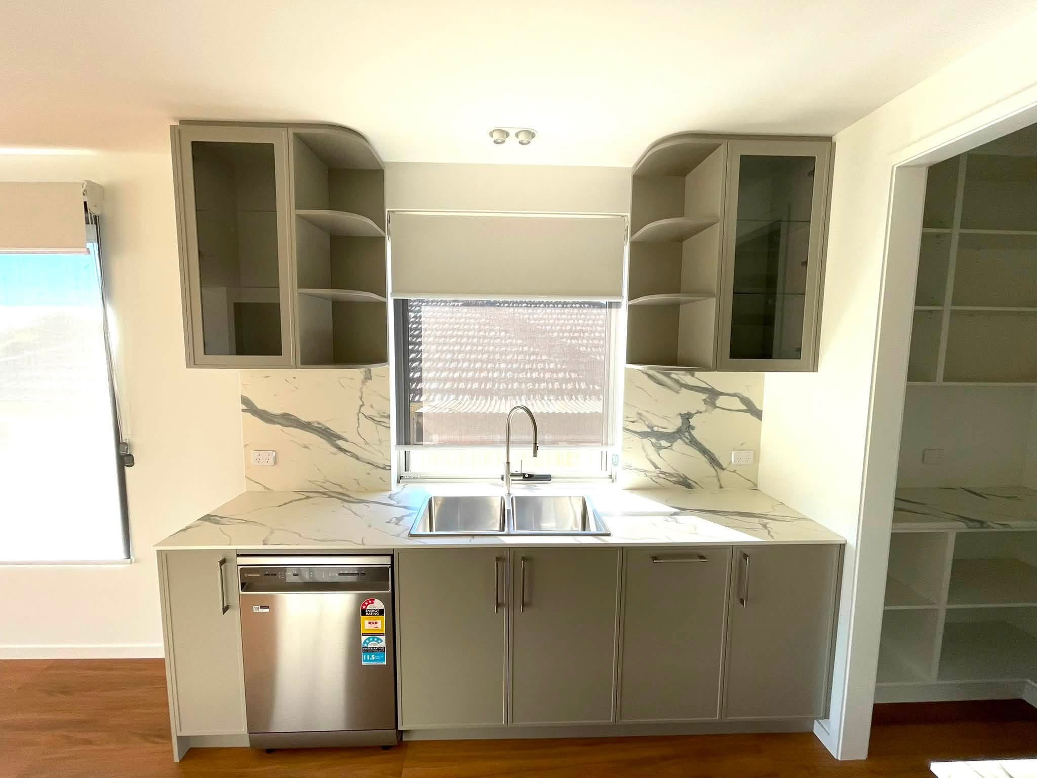 Sage green kitchen sink run with glass-front overheads, built by Central Coast Joinery